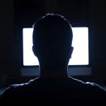 Man seated in front of computer monitor at night