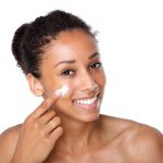 Attractive young woman applying cream on face