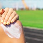 Fitness woman is applying sunscreen on her shoulder before training at the stadium. Protect your skin during sport activity